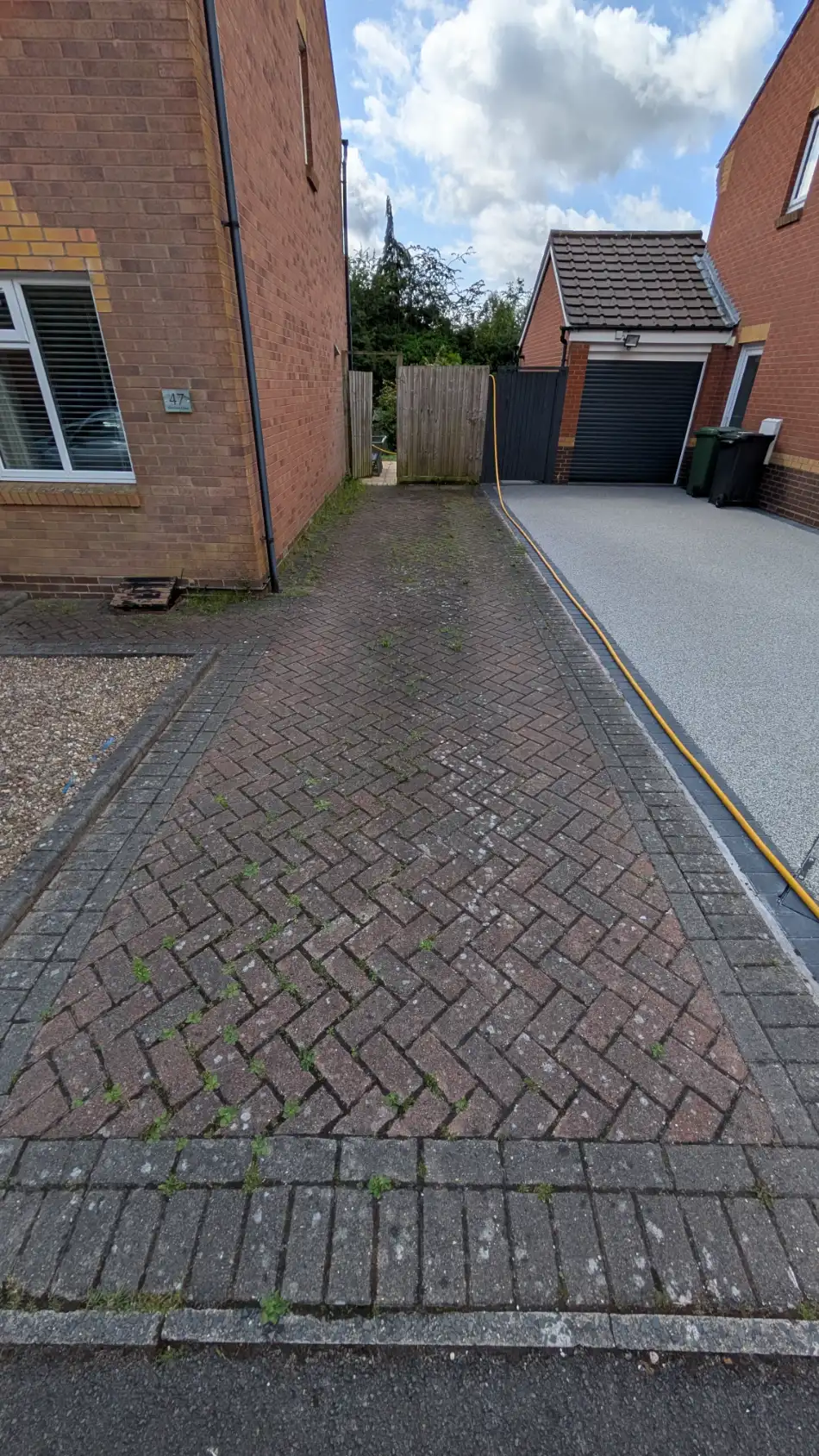 Block-paved driveway and side path before cleaning, with weeds growing in the joints
